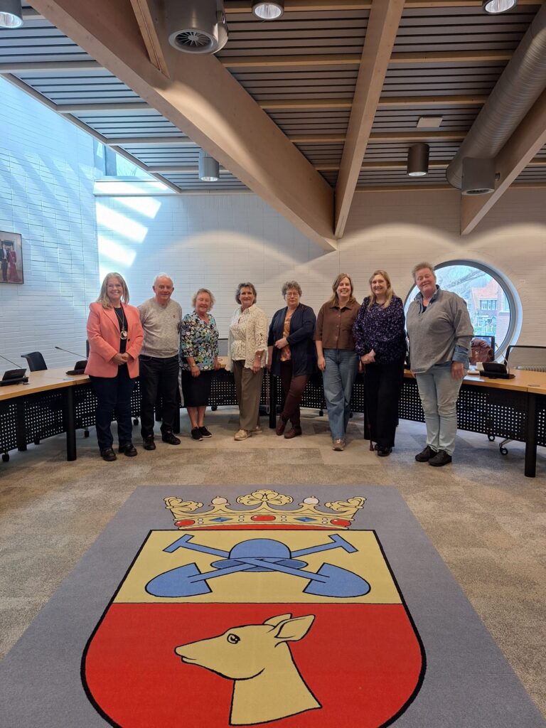 de aanwezigen van de ALV staan in de raadszaal van Bodegraven waar op de grond het logo in het tapijt is verwerkt
